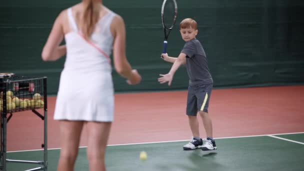 Entrenador y niño pequeño con raqueta practicando hit en la cancha — Vídeos de Stock