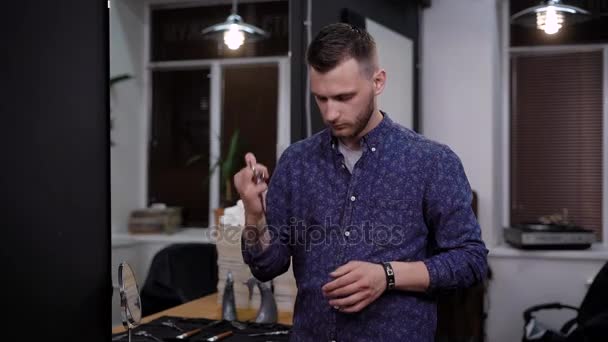 Male barber twisting and spinning scissors in his hand like a pro. Then he looks on the cutting surface of the scissors — Stock Video