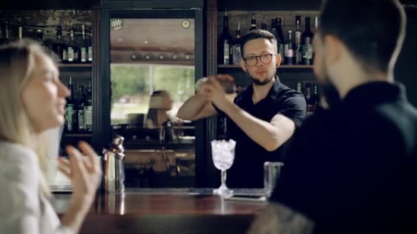 Милый и молодой бармен пожимает шейкер с коктейлем в руках, люди у стойки бара, которые аплодируют мастерству общественного питания — стоковое видео