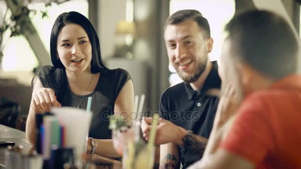 Jovens bonitos e adultos passam tempo em um pequeno bar, a empresa se comunica uns com os outros, homens e mulheres que bebem coquetéis riem e se divertem — Vídeo de Stock