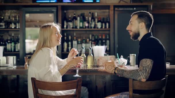 A happy couple laughing while communicating with each other, a young woman with blond hair tells a funny story, a bearded man drinks a long cocktail — Stock Video