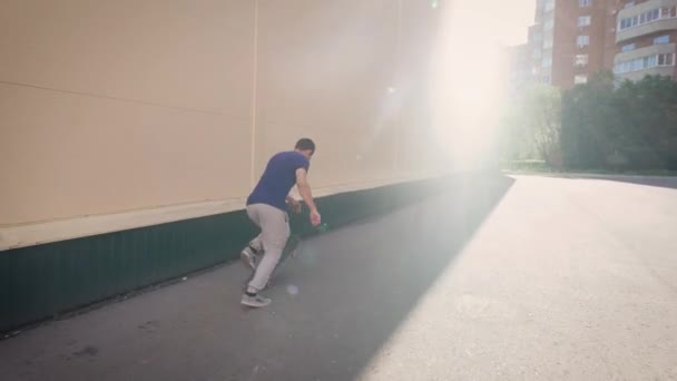 Jeune passionné de sports extrêmes passant son temps libre à patiner dehors dans la journée d'été. Garçon vêtu de vêtements décontractés glissant le long du mur et sautant par-dessus la barrière sur le skateboard dans la rue . — Video
