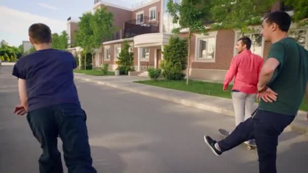 Вид сзади на трех друзей, катающихся на скейтбордах в летний день. Молодые люди в повседневной одежде катаются по улице. Любители экстремального спорта проводят время на свежем воздухе, демонстрируя здоровый образ жизни . — стоковое видео