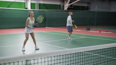 Mutlu çift kapalı sarayda tenis oynamaya görüntüsü. Gençlerin spor kıyafeti giymiş zaman birlikte eğitim rekreasyon alanı içinde harcama vardır. Erkek ve kadın tutarak raketleri ve topları vurmak.