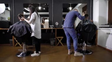 Çalışma oturup müşterileri ile kadın ve erkek kuaförleri arkadan görünüm berber kesme burunları ile kaplı. Genç kadın ve hairclippers kullanarak ve müşteriler başkanları tıraş yakışıklı adam.