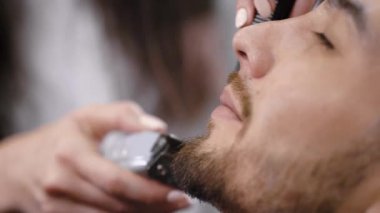 Genç sakallı adamın yüzü şık berber, Kuaför tarafından saç kesimi almak yakın. Sakal ve bıyık yakışıklı hipster için düzeltici Başlarken mükemmel şekli kullanarak eller görüntüsünü.