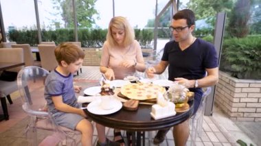 Baba ve anne oğlu ile masaya oturup oğulları restoranda dilim pizza sağlar