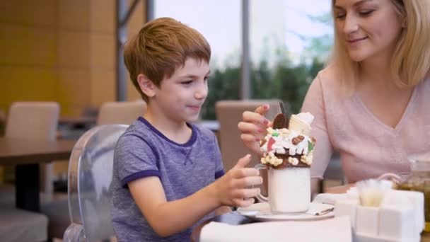 Giovane ragazzo è felice con un grande dessert ha ottenuto e dare la sua bella madre a gustarlo un po ' — Video Stock