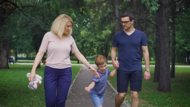 Feliz família jovem alegre está se divertindo ao ar livre, no parque de verão. Mãe, pai e filho estão rindo e curtindo a natureza lá fora. Dia ensolarado, bom humor — Vídeo de Stock