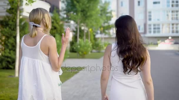 Duas mulheres incríveis vestindo vestidos brancos estão andando por um beco e falando pacificamente sobre algo — Vídeo de Stock