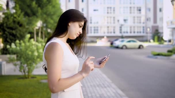 Junge charmante Frau steht am Straßenrand und sieht sich im Sommer Fotos ihrer Selfies an — Stockvideo