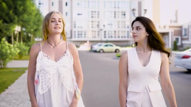 Dos mujeres de buen aspecto con vestidos blancos están caminando por un callejón, hablando de la vida y los eventos — Vídeo de stock