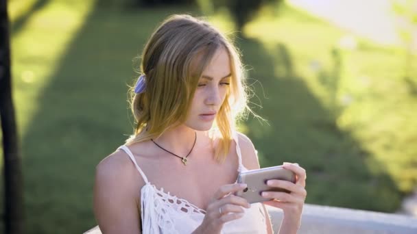 Retrato de menina bonita vestida de vestido branco segurando seu telefone celular, usando a internet, passando por feed de notícias — Vídeo de Stock