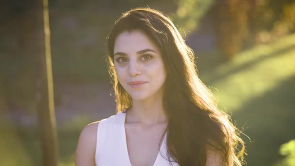 Joven mujer sonriente increíble en vestido blanco se sienta en la becnch en el parque y brilla con belleza en las luces de rayos . — Vídeo de stock