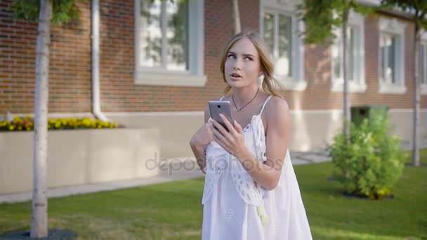 Jovem mulher atraente vestindo vestido de renda branca vai para uma caminhada para falar com sua amiga no videochat — Vídeo de Stock