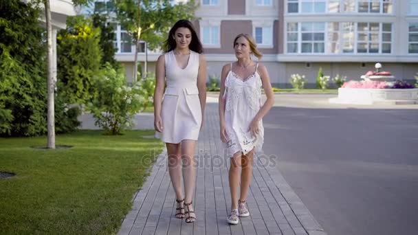 Zwei gut aussehende Frauen in weißen Kleidern gehen eine Gasse entlang und sprechen über das Leben und die Ereignisse — Stockvideo