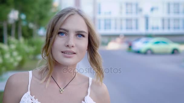 Mulher loira jovem e incrivelmente bonita com olhos azul-celeste em vestido branco caminha pelo beco e sorri bem enquanto penteia o cabelo . — Vídeo de Stock