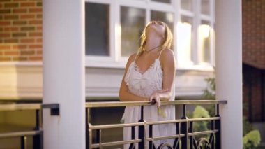 Gündüz vakti yazlık balkon korkuluk, poz ve flört siyah metal ince sarışın genç duruyor