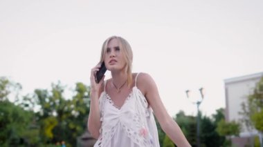 Kızgın sarışın konuşuyor yaz günü, küfür ve bağırarak, şehirde telefonla kamera hareket