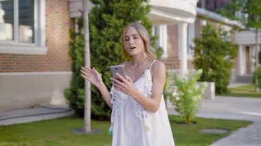 Genç sarışın video yapıyor çağrı gülümseyen ve konuşurken güneşli yaz günde bir sokakta geziniyor