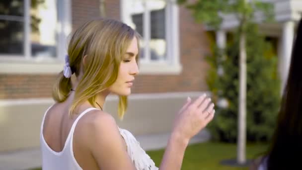 Unga blonda kvinnan är promenader i city i solig dag och pratar med vän, halvt varv Filmning — Stockvideo