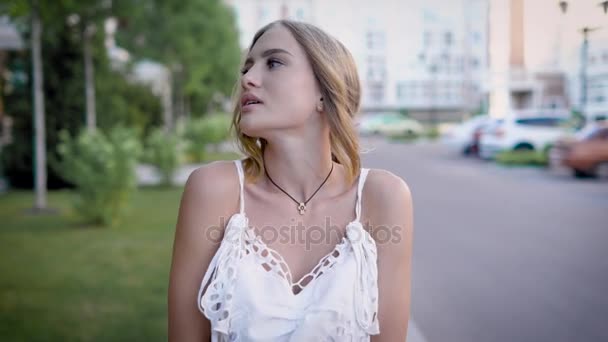 Young attractive blonde is walking and looking to a camera in summer day on street, touching shoulders — Stock Video