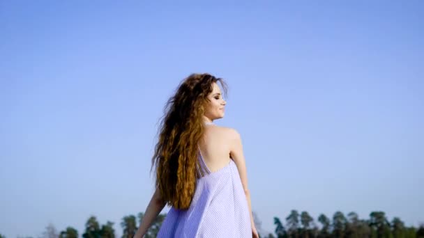 Una mujer feliz y joven disfruta de un día de verano al aire libre, agita las manos a los lados, protege el sol con las manos y ríe — Vídeo de stock