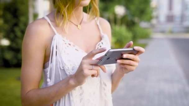 Крупним планом знімок жіночих рук, який тримає смартфон, дама дивиться на соціальні мережі своїх друзів, вона на вулиці — стокове відео
