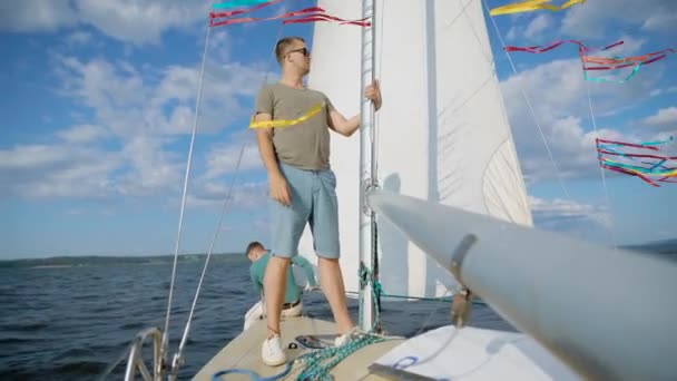 Stilig ung man, som är captait av denna yacht, dra repet att segla ut i havet på sommaren — Stockvideo