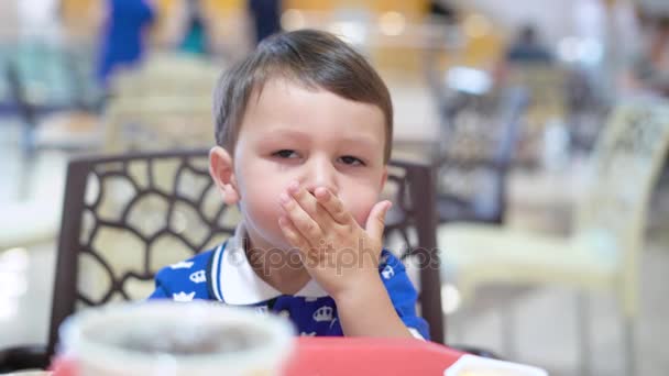 Pequeño chico de pelo oscuro está sentado en una silla y comer papas fritas con salsa en el restaurante — Vídeos de Stock