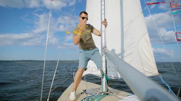 Мужчина-искатель приключений позирует на современной парусной лодке, глядя вдаль на солнце — стоковое видео