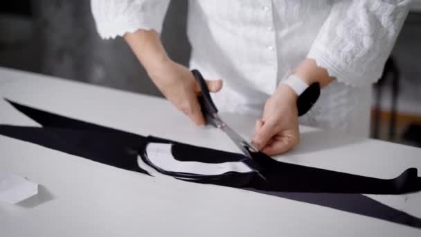 Close up van vrouwelijke handen met een pin kussen zwarte doek knippen met een schaar op witte tafel. Afbeelding van het lichaam van een vrouw die permanent in de afstemming van de studio en het uitsnijden van materiaal voor de inzameling van kleding. — Stockvideo