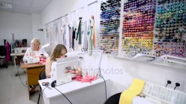 İki kadın seamstresses dikiş makinesi studio terzilik içinde masalarda oturan üzerinde çalışıyor. Çekici needlewomen giyim moda atölye çalışma yerinde dikiş.