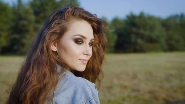 Jonge stijlvolle lachende meisje met lang haar en prachtige bruine ogen met een wandeling in het veld en langzaam verandert terug — Stockvideo