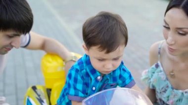 Genç izlerken küçük çocuk oyuncak arabası Street anne. Mutlu anne ile küçük oğlu yeni binmek için ona yardım vakit araba Sokağı'nda oynamak..