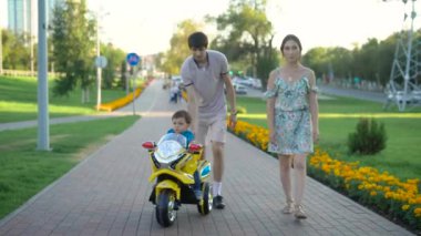 Aile Park oğlu oyuncak arabası ile vakit geçirmek. Küçük çocuk arabası oyun yakınındaki yaz Park'ta yürüyordunuz veliler ise.