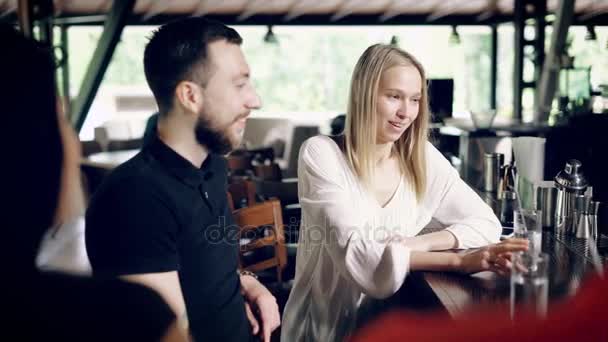 Male and female friends in cafeteria sitting at a bar counter in summer day with barman working.Beautiful girl telling story to companion laughing and gesticulating with silhouettes in the foreground. — Stock Video