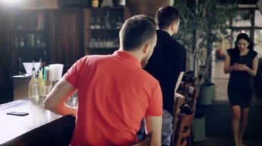 Gündelik elbise bar sayacı kafede oturan genç erkeklerde görüntüsü. Yakışıklı adamlar ayakta ve kucaklayan ve onları sıcak öpüşme gelen kadın arkadaşlarını davet edici masada oturan.