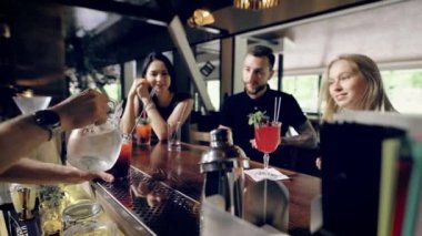 Bardaki müşteriler taze kokteyller yapıyor barmen izliyor. Köşede oturan insanlar içecek hazırlama bir barmen el kapatın. İki kız için onların erkek içki kılmayı arıyorum
