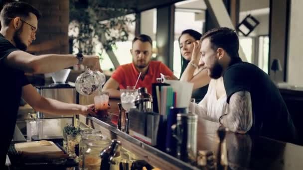Kunder i baren som ser på bartender som drikker fersk cocktail. Tett i hendene på en bartender som lager drikke til folk som sitter. Vakre jenter med smarttelefoner som vil lage drinker . – stockvideo