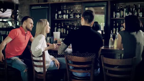 Image d'amis assis au comptoir du bar pendant que le barman travaillait de l'autre côté de la table en bois avec étui de fenêtre en arrière-plan. Compagnie de quatre personnes ayant rompu ensemble parlant et riant . — Video