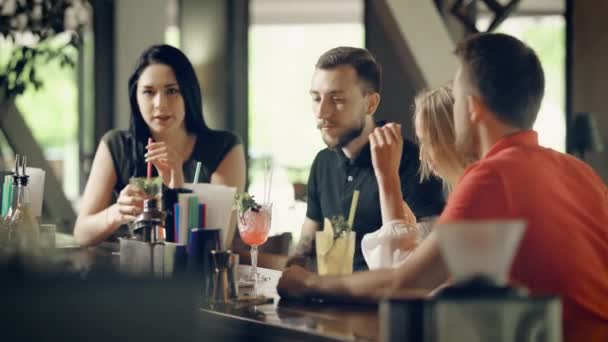 Dwóch młodych par picia koktajli w barze licznika. Czterech studentów, którym spędzać czas razem z okazji święta. Firma mężczyzn i kobiet siedzi i śmiejąc się radośnie. — Wideo stockowe