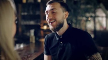 Genç kadın arkadaşı ile restoranda oturan rahat siyah t-shirt erkekte sakallı. Kadın karşısında onu dinlerken ve gülerek hippi. Bardaki kız arkadaşı ile vakit adam.