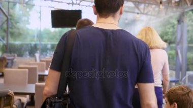 Restoran Menü ile ayakta ve Konuklar genç erkek garson kapatın. Mutlu bir aile birlikte vakit için kafede geliyor. Baba, anne ve oğlu olacak ve masaya oturarak.