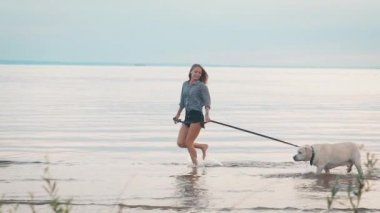 kadın büyük labrador büyük nehir kıyısında bir leash üzerinde akşam saat içinde gülümseyen ve gülerek yürüyor