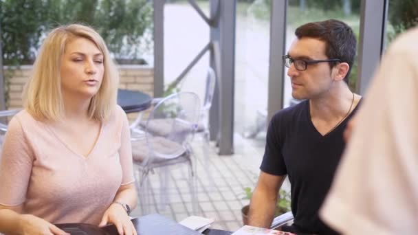 Eine junge Mutter bestellt die Hauptgerichte im Restaurant, neben ihrem Mann und einem kleinen Sohn, der am Tisch sitzt und sich die Speisekarte ansieht — Stockvideo