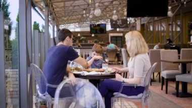 Bir restoranda genç bir aile akşam, bir kadın çay içen kocası tarafından fotoğraflandı, çocuklarının bir milkshake bir saman içiyor.