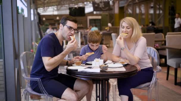 Счастливая семья обедает в ресторане, муж и жена заказали пиццу, их маленький сын доволен вкусным выбором своих родителей — стоковое видео