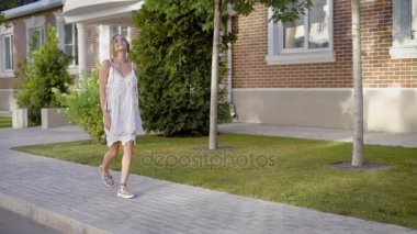 Neşeli kadında büyüleyici kaldırım boyunca yürüyüş ve kameraya bakarak gündelik elbise.