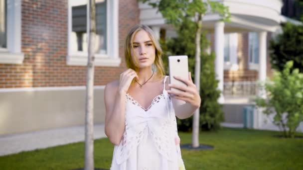 Junges sinnliches Mädchen in Weiß macht Selfie, während sie allein auf der Sommerstraße posiert. — Stockvideo